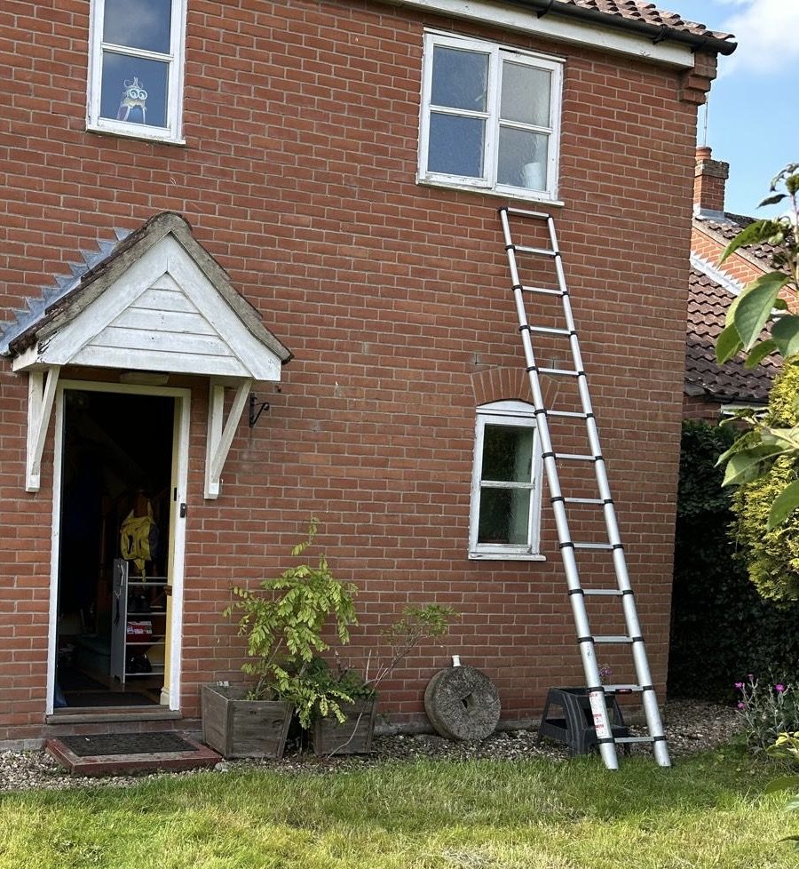 Front view of a red brick house in Norwich with an old timber porch canopy, single-glazed timber windows, and a ladder leaning against the wall prior to renovation.
