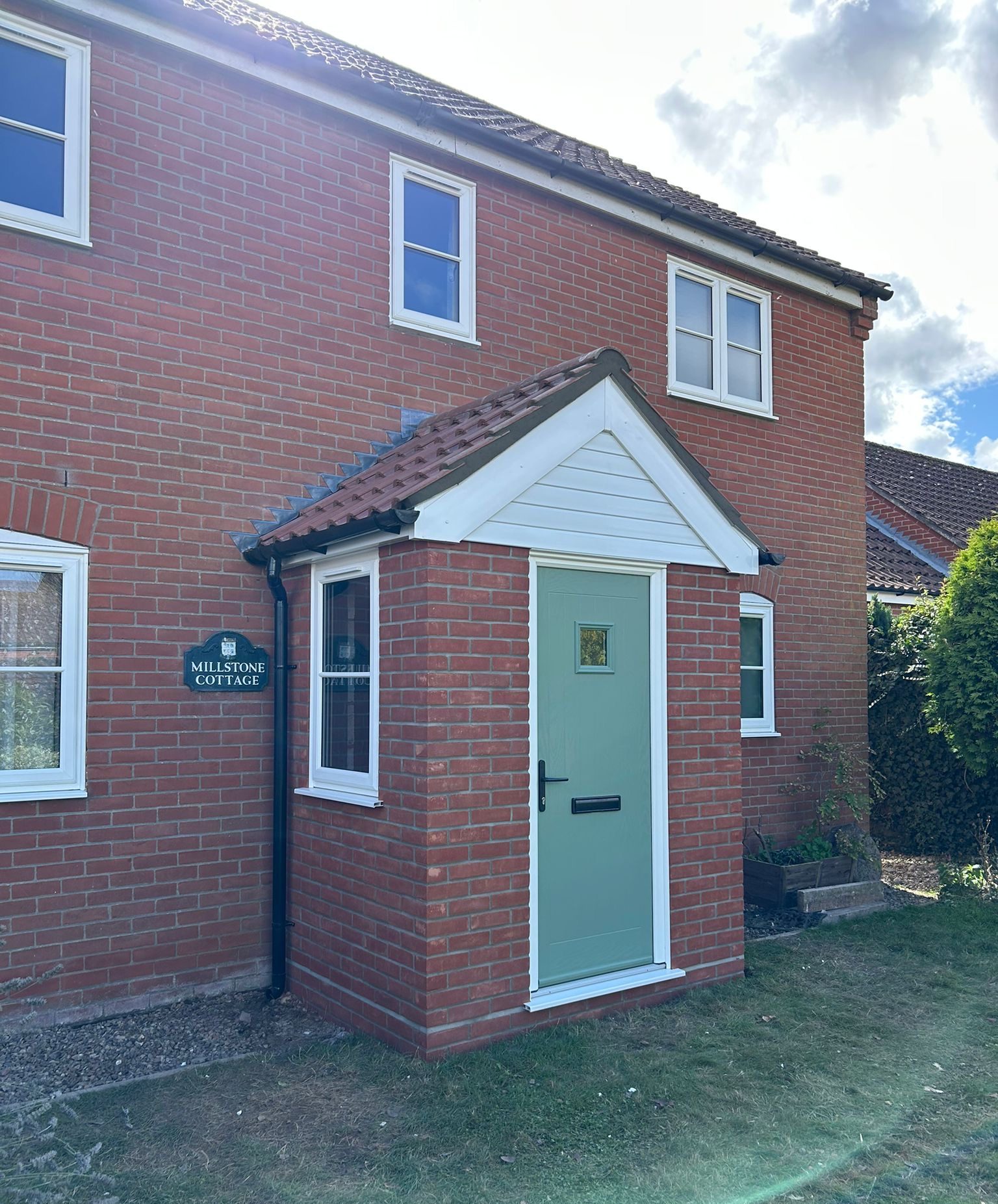 Front view of a completed brick-built porch with a sage green composite front door and uPVC windows, fitted to a red brick house in Norwich, Norfolk.